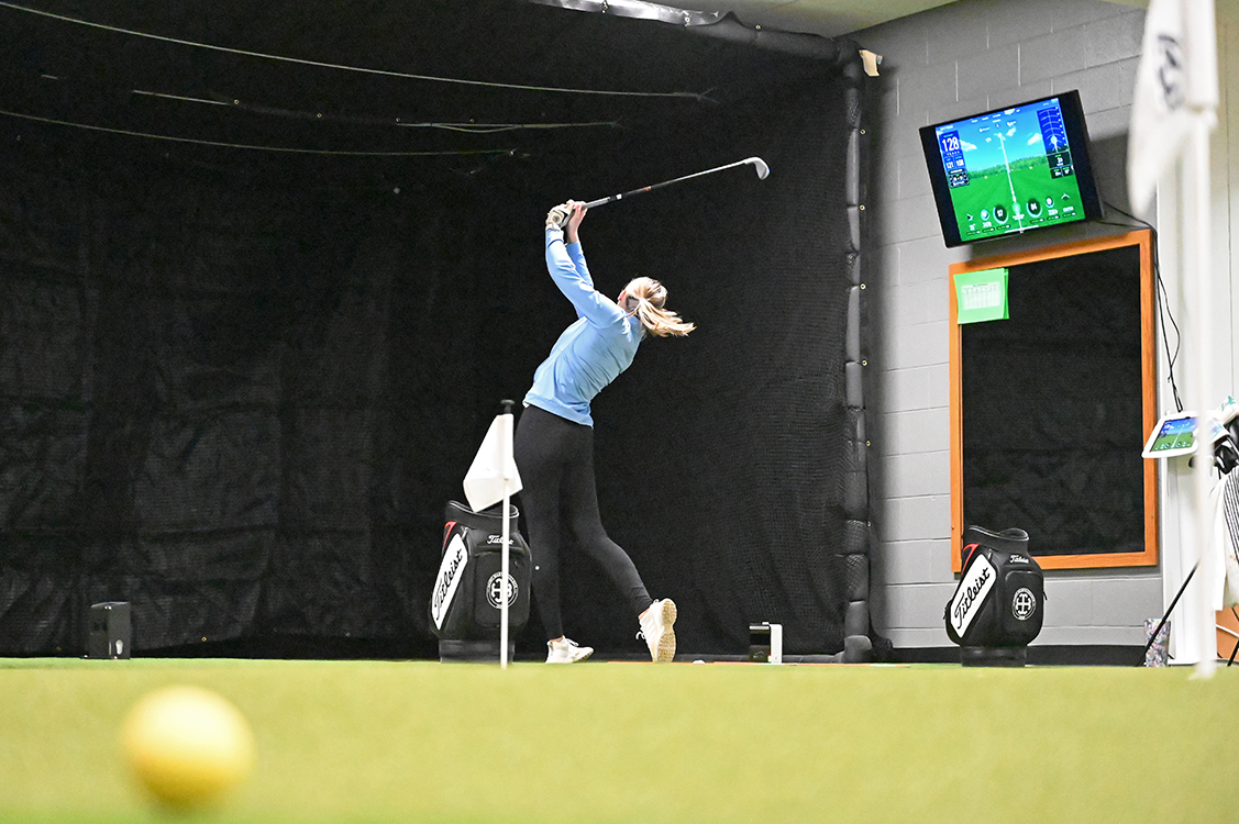 A golfer hits a ball into a black netted background while using the simulator.