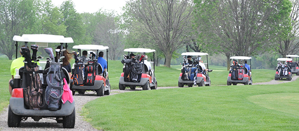 A line of golf carts drives out along a gravel path to begin the golf outing.