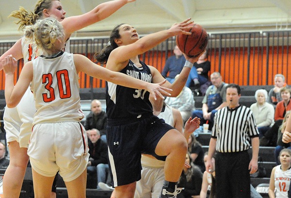 Giavanna Paradiso, wearing a navy blue uniform, goes up for a layup with two defending players in white next to her to the left.