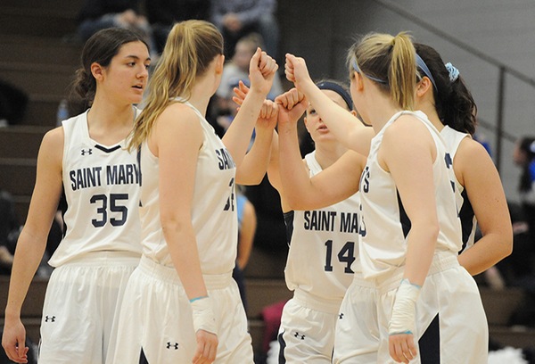 Five Saint Mary's basketball players wearing white uniforms huddle together with their hands together prior to the start of the game.