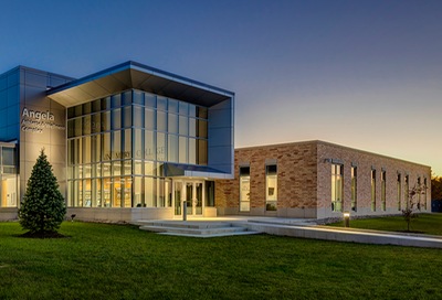 Exterior view of the north entrance to Angela Athletic and Wellness Complex. Photo taken at sunset of primarily brick building with high glass entrance all internally illuminated.
