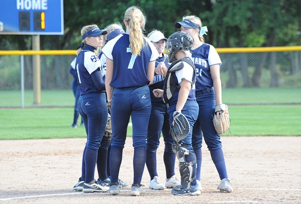 Six players, all wearing navy blue uniforms, huddle up prior to the start of an inning.