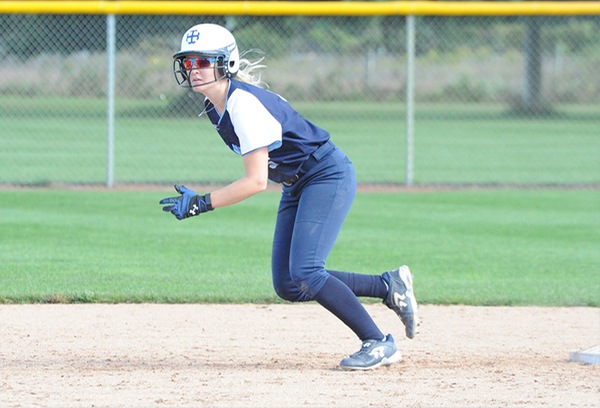 Megan Knudsen, wearing a navy blue uniform with a white helmet, begins to run from second base.