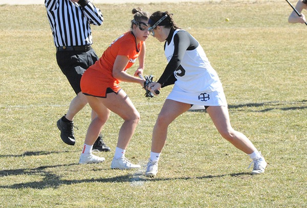 Kate Kelly, pictured on the right in a white uniform, prepares for a draw control against an opposing player in an orange uniform.