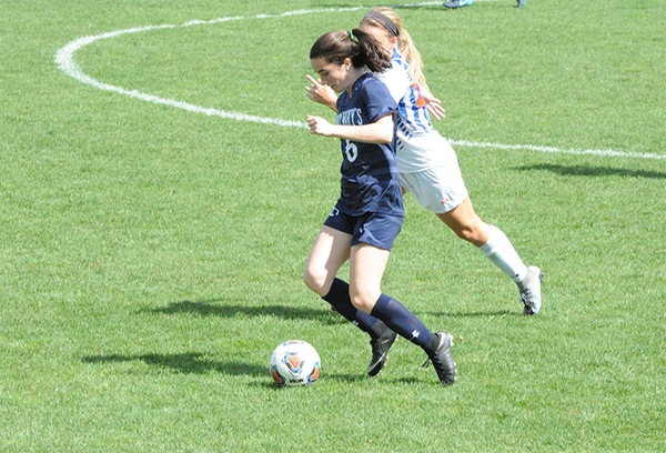Sophie Bubnar, in dark blue uniform, plays the ball forward with a defensive player in white visible in the background.