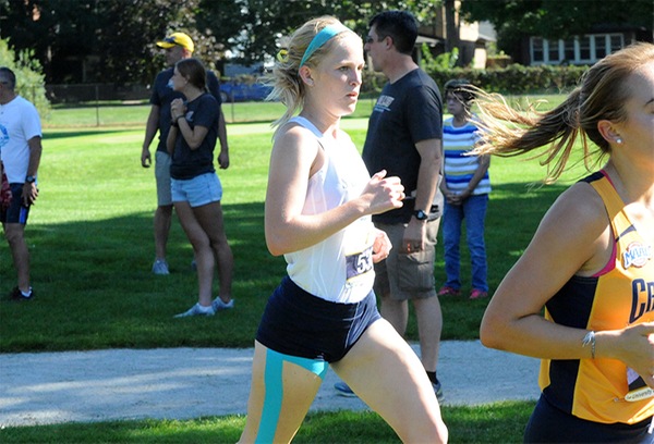 Katie Glenn, wearing a white tank top and a light blue headband, runs with several people in the background.